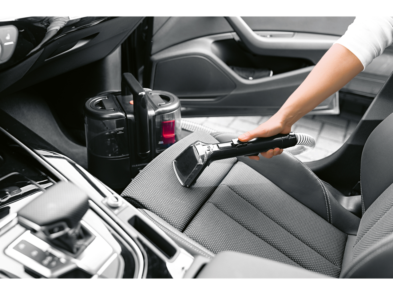 Mulher a limpar um banco de carro com um aspirador de estofos e carpetes Cleanmaxx.