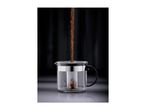 Tea leaves pouring into a glass teapot with an infuser on a dark background.