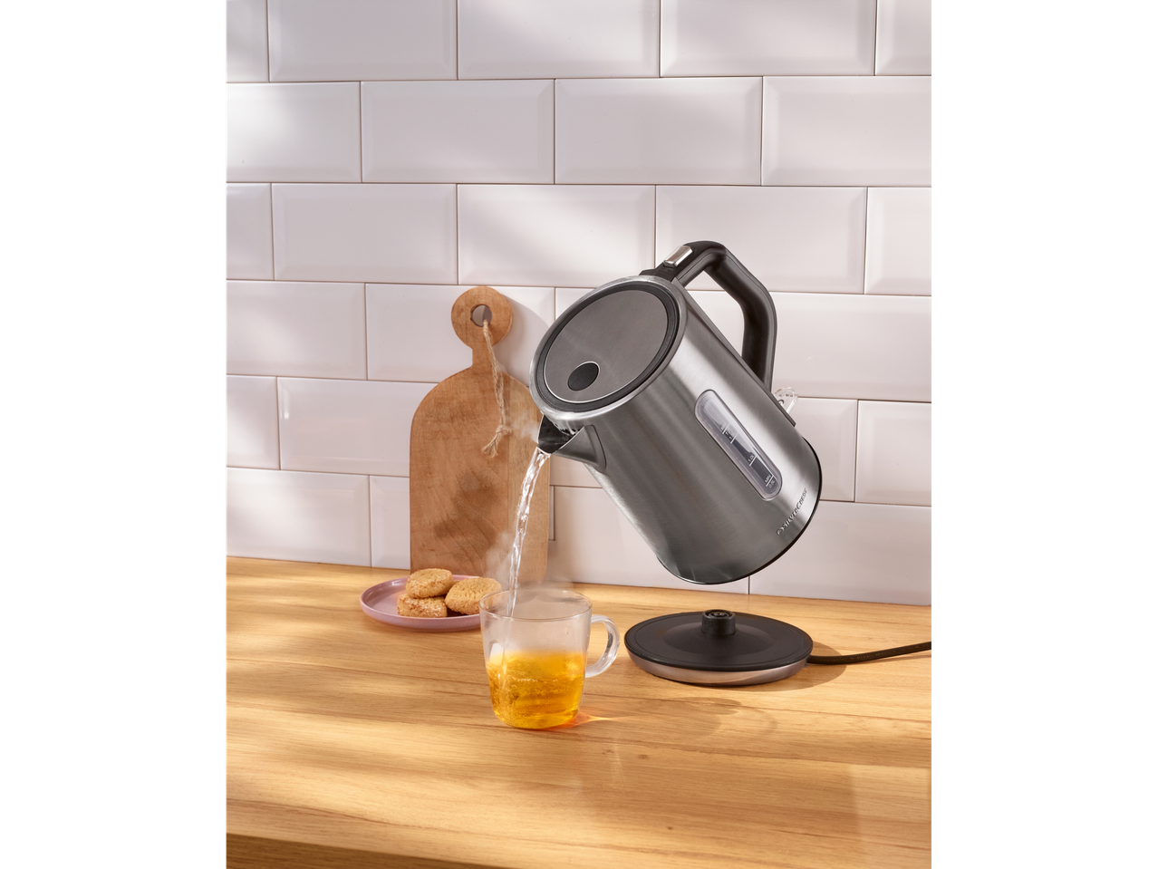 Silvercrest® električno kuhalo za vodu ulijeva vruću vodu u šalicu čaja s keksima.
