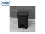 A black Addis step-on trash can sits on a grey floor.