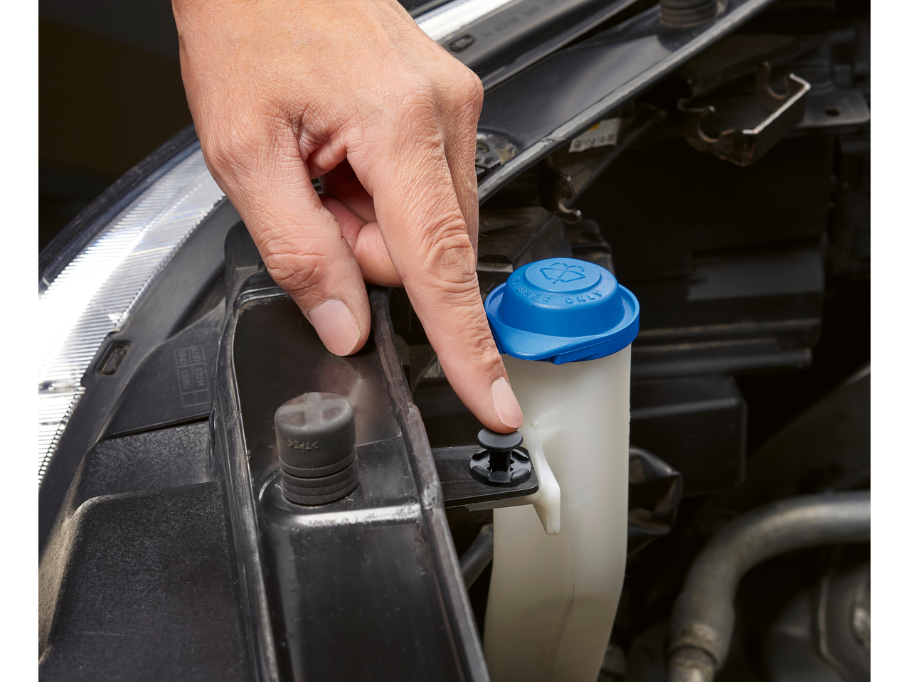 Hand pressing a Parkside® fastening clip on a car's windshield washer fluid reservoir.