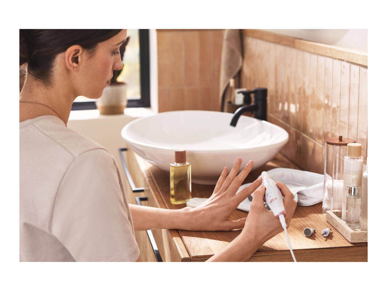 Woman using an electric nail file for a manicure at a bathroom vanity.
