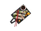 Fresh spring rolls arranged on a black slate with dipping sauce and chopsticks.