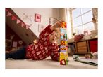 Toddler in a festive jumper playing with stacking blocks on a rug in a decorated room.