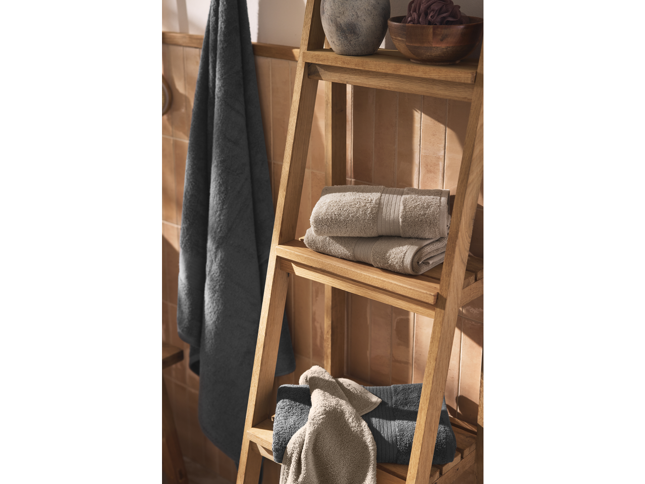 Toalhas LIVARNO cinzentas e bege numa prateleira de madeira, com uma toalha pendurada