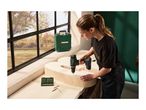 Woman drilling into a wooden letter with a cordless drill, with a tool case and drill bits nearby.