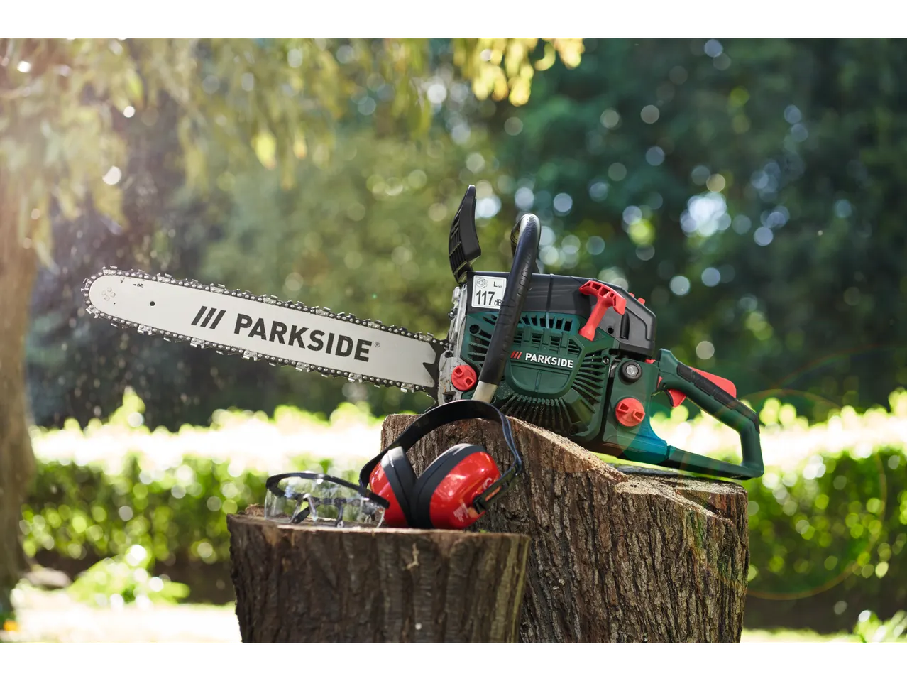 Motosserra Parkside com óculos e protetores auriculares em um toco de árvore.