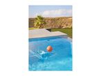 Orange basketball splashing in a blue swimming pool with a sunny landscape.