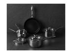 A set of stainless steel saucepans and a frying pan with lids on a dark background.