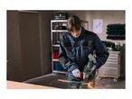A person wearing safety gear uses a cordless angle grinder to cut metal in a workshop.