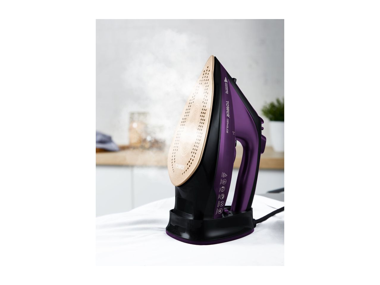 Purple and black steam iron with a gold soleplate, emitting steam over white fabric.