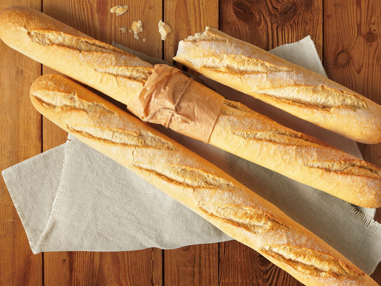 Три пресни багети върху ленено платнище, дървена маса.
