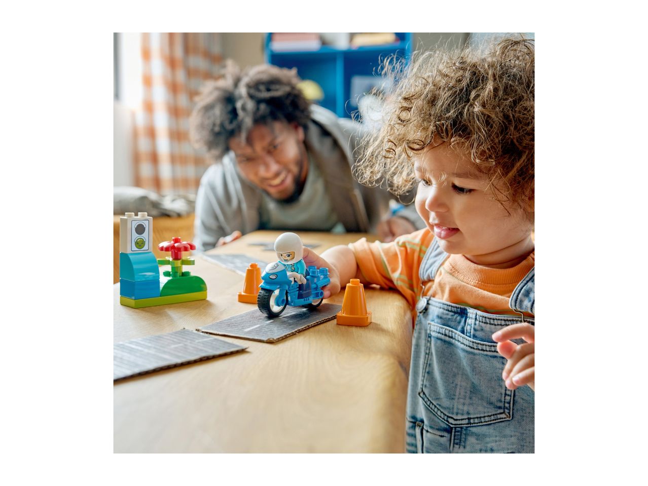 A child and adult playing with building blocks, including a toy motorcycle and traffic light.