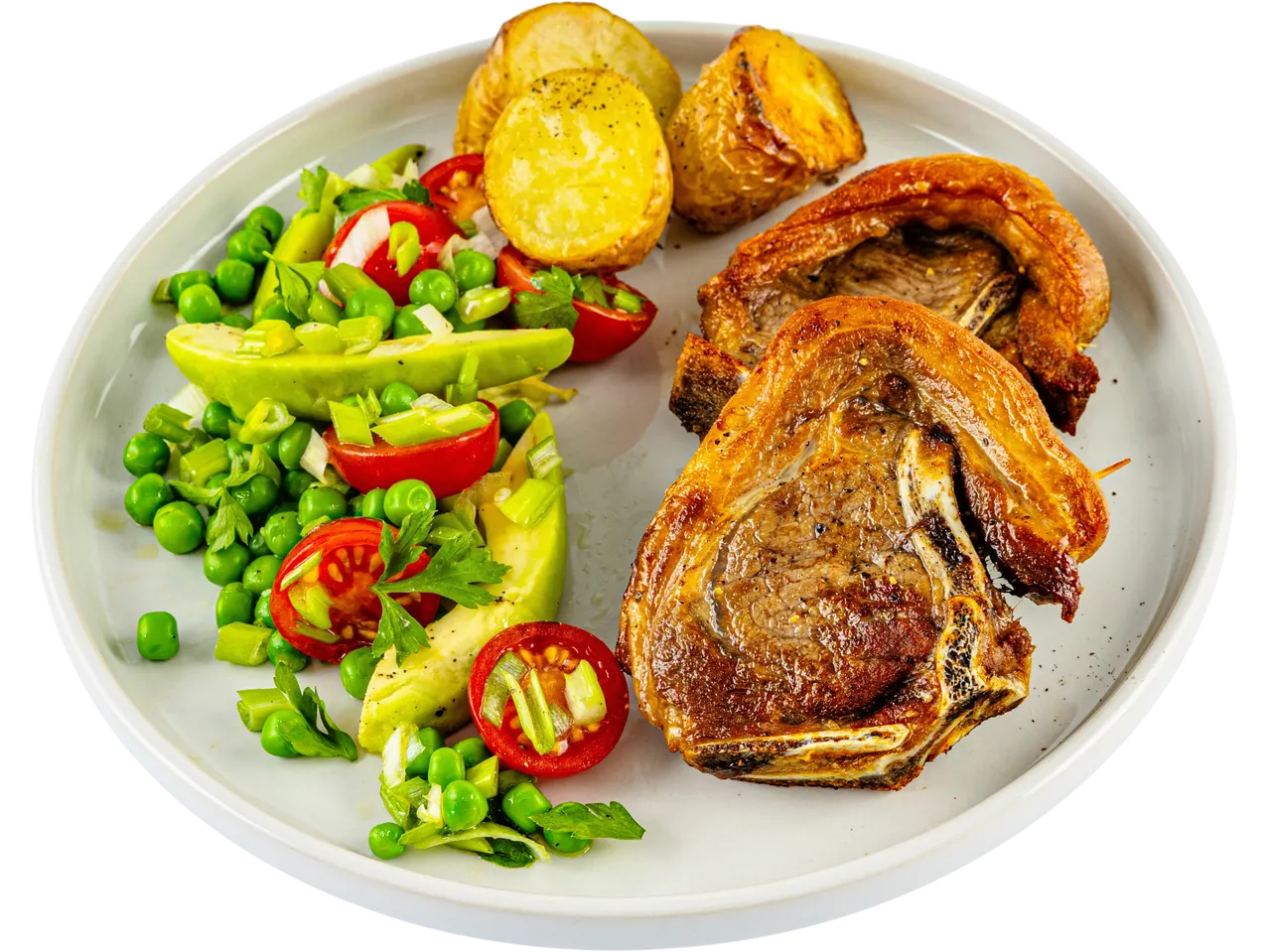 A plate of roasted lamb chops served with roasted potatoes and a fresh pea, avocado, and tomato salad.