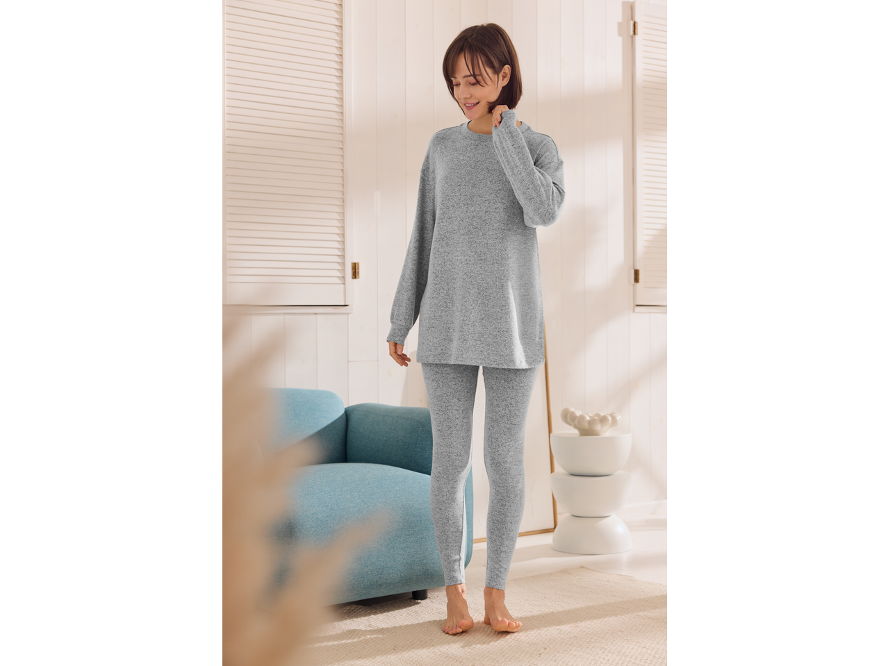 Mulher em pijama cinzento confortável Esmara, de pé numa sala luminosa.