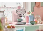 A pink SilverCrest espresso machine makes coffee in a pastel kitchen setting.