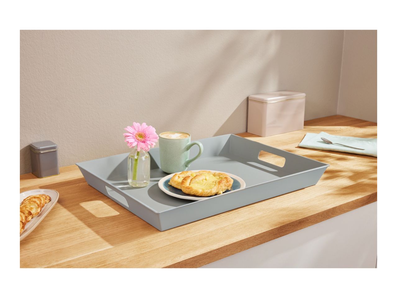 A breakfast tray with a coffee mug, pastry, and flower on a wooden counter.