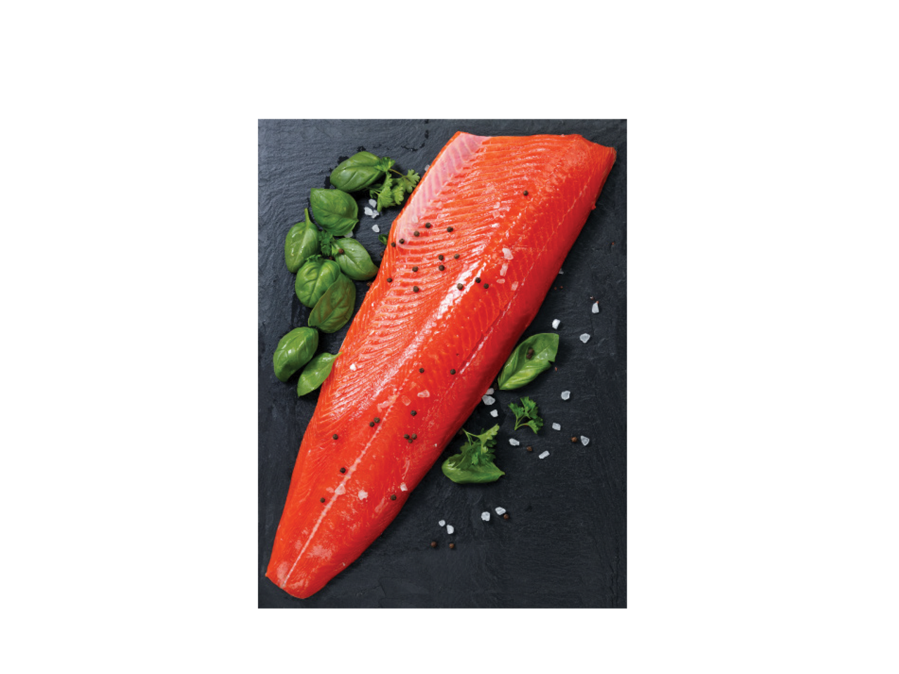 Jēla laša fileja ar melnajiem pipariem, jūras sāli un svaigu baziliku uz tumša dēlīša.