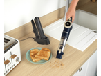 Handheld vacuum cleaner cleaning crumbs from a wooden kitchen counter next to a toaster and toast.