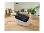 Black battery pack charging on a light wooden table in a modern living room.