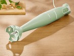 Ein mintgrüner Silvercrest Stabmixer liegt auf einer Holztischfläche.