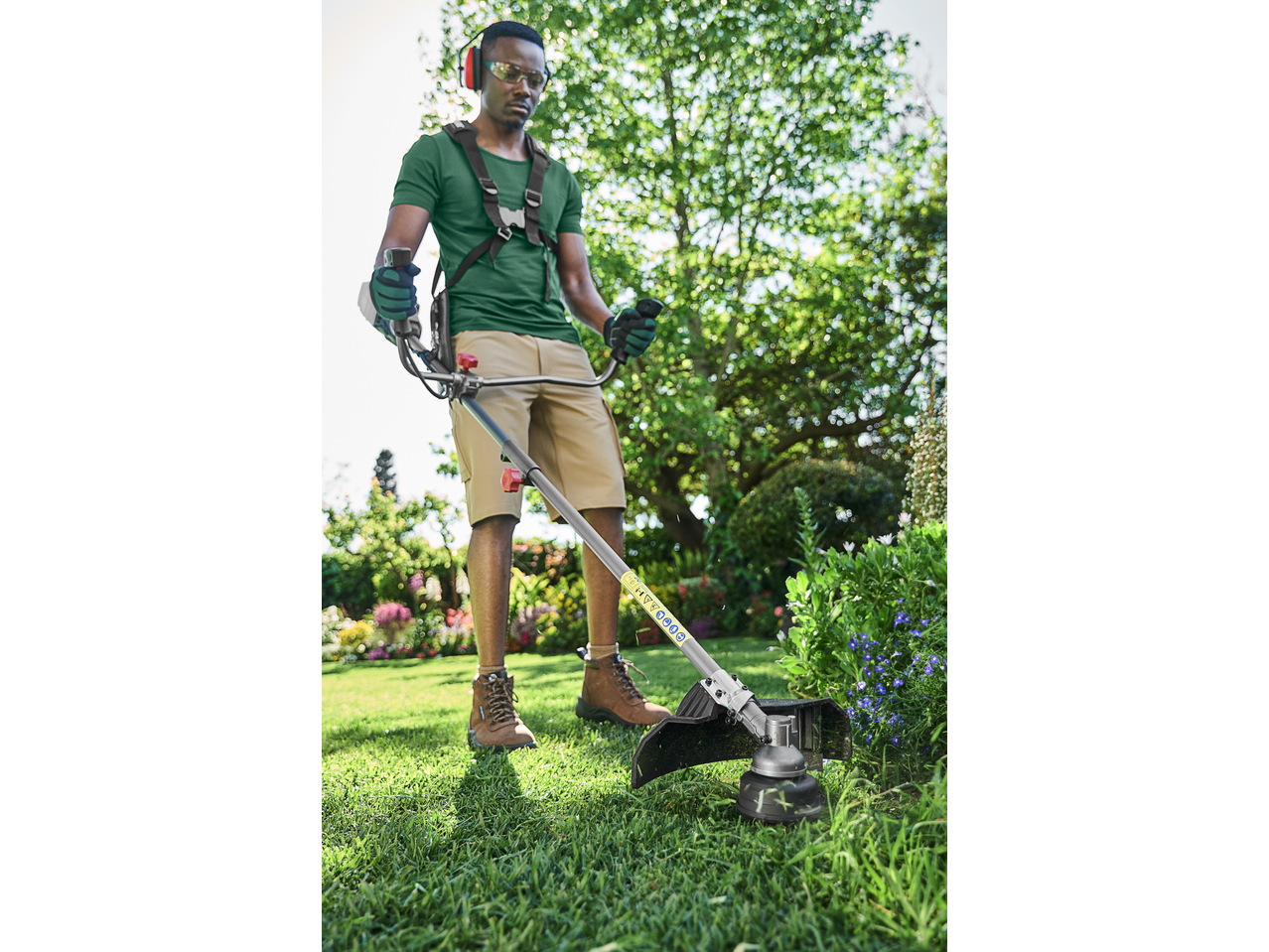 Man using a grass trimmer in a garden, wearing safety glasses and ear protection.