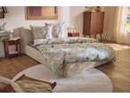 Quarto com cama de casal com roupa de cama floral, mesas de cabeceira e armário de madeira.