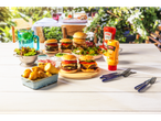 Burgers, potatoes, corn, and Batts sauces on a picnic table.