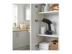 Handheld garment steamer and cleaning supplies in a white cabinet, with a kitchen in the background.