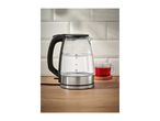 Glass electric kettle with water and a cup of red tea on a wooden counter.