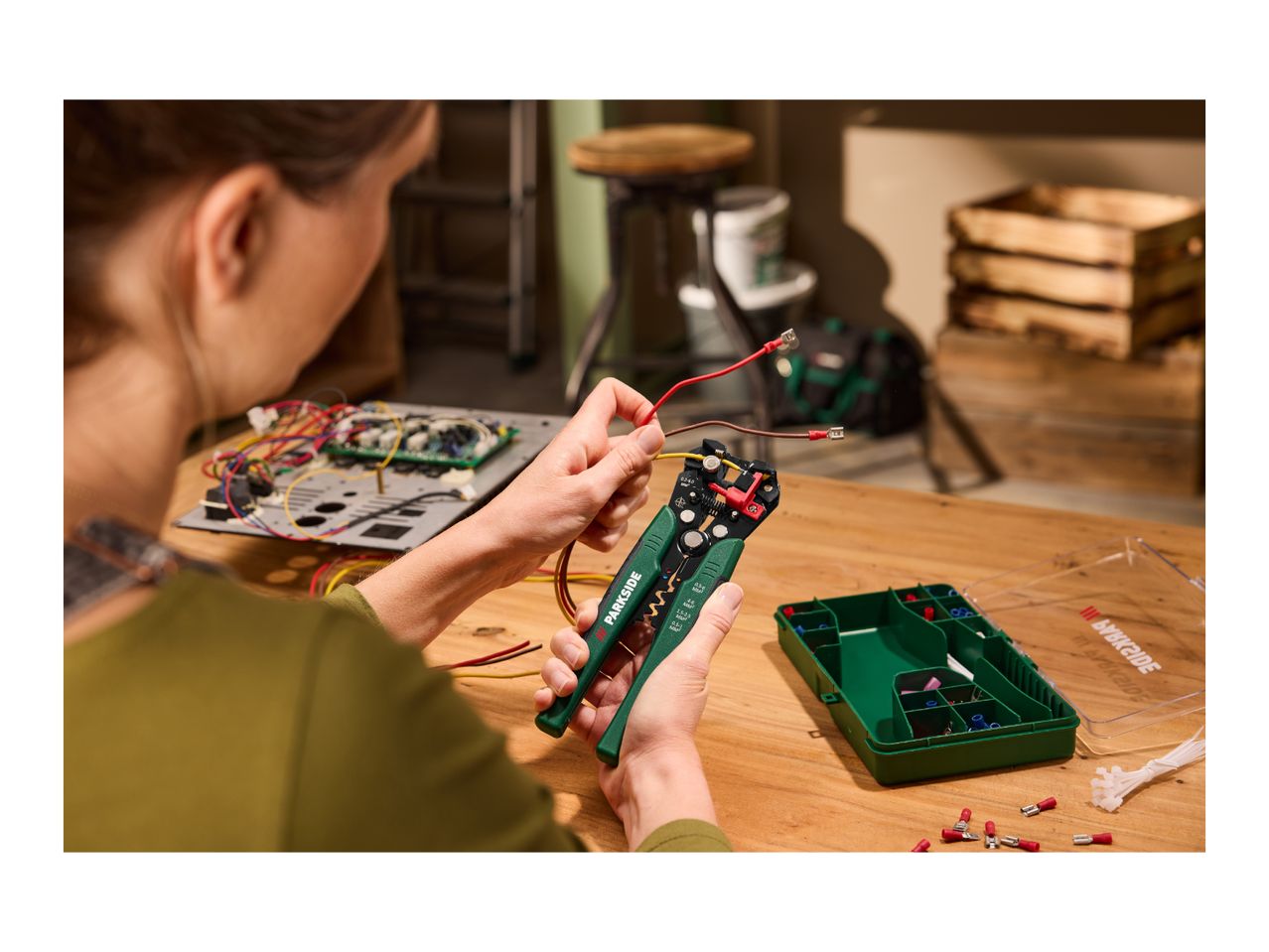 Person using wire strippers to prepare electrical wires, with a component box nearby.