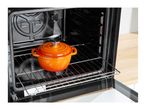 An orange pot with a lid inside a black oven on a metal rack.