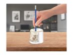A hand inserts a blue pencil into a white and beige rotary pencil sharpener on a wooden table.