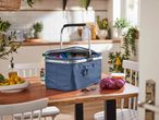 A blue cooler bag filled with groceries on a wooden table in a kitchen.