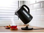 Black Silvercrest electric kettle pouring hot water into a teacup.