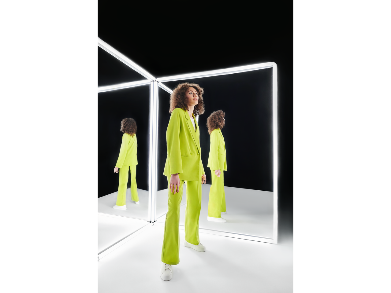 Modelo com terno amarelo neon e tênis brancos, refletido em espelhos.