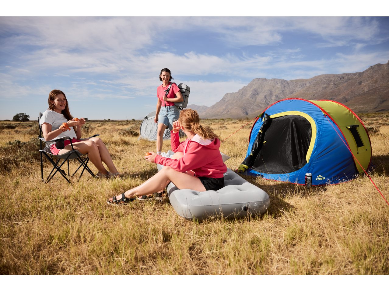 Three women camping with a CRIVIT tent and a CRIVIT Camping Air Bed in a field.
