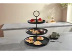 Suport etajat negru cu prăjituri și o ceașcă de cafea pe un blat de bucătărie