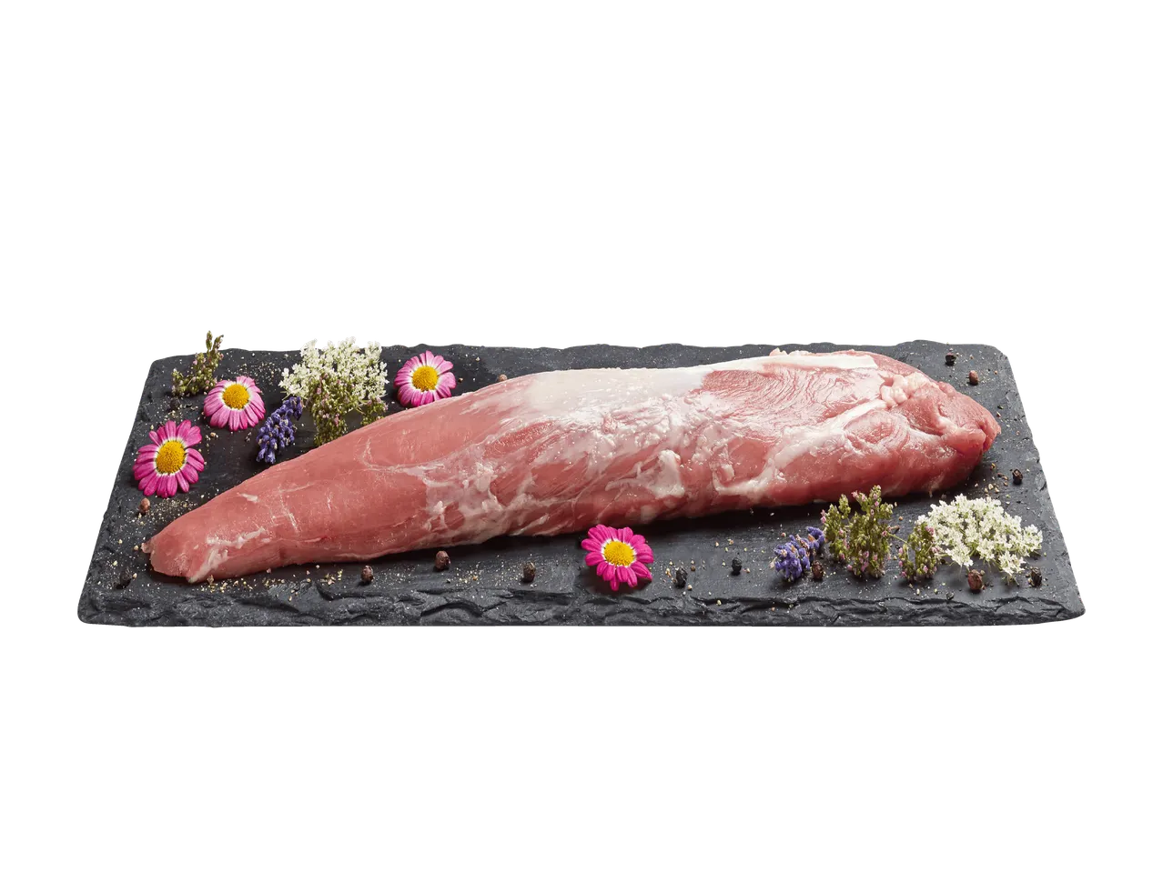 Filetto di maiale crudo su un tagliere di ardesia con fiori e spezie.