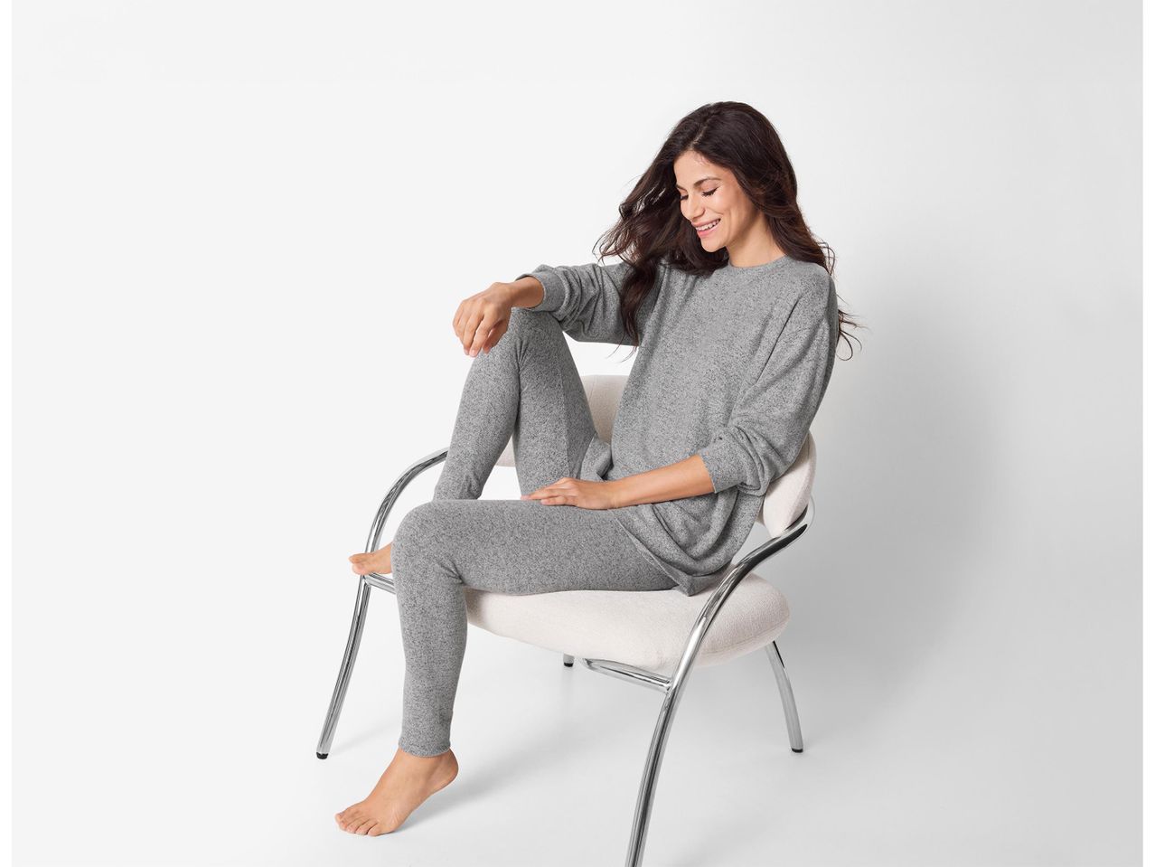 Nő szürke szabadidőruhában ül egy széken, mosolyogva.