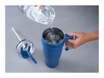 Water being poured into a blue tumbler with ice, next to its lid and straw.