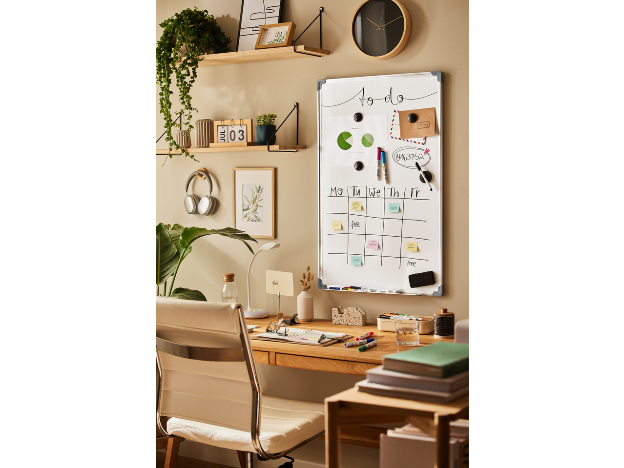 A home office desk with a whiteboard showing a weekly planner, markers, and accessories.