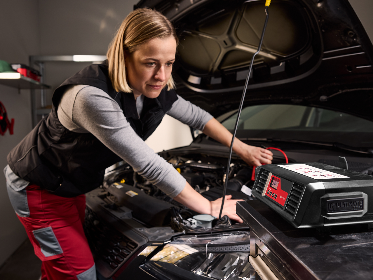 Жена зарежда акумулатор на кола с устройство за зареждане на акумулатори.