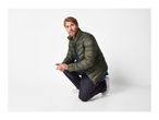 Man in an olive green puffer jacket, blue denim shirt, and dark jeans, crouching.