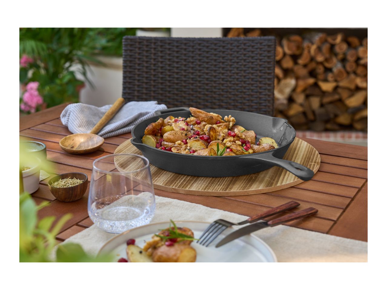 Cast iron skillet with roasted potatoes, walnuts, and pomegranate on an outdoor table.