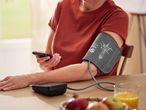 A person using a blood pressure monitor on their arm while holding a smartphone.