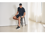 Man using a CRIVIT Mini Massage Gun on his thigh while sitting on a stool.