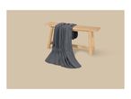Dark grey blanket draped over a light wooden bench on a beige background.