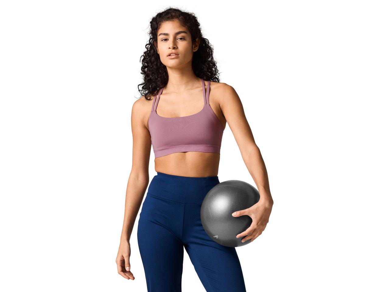 Woman in a sports bra and leggings holding a small exercise ball.