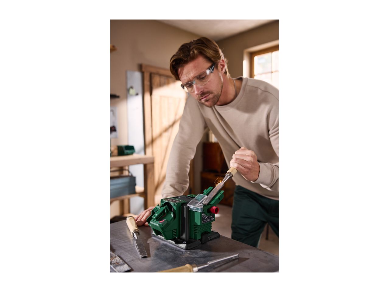 Man sharpening a chisel with an electric sharpener, sparks flying.